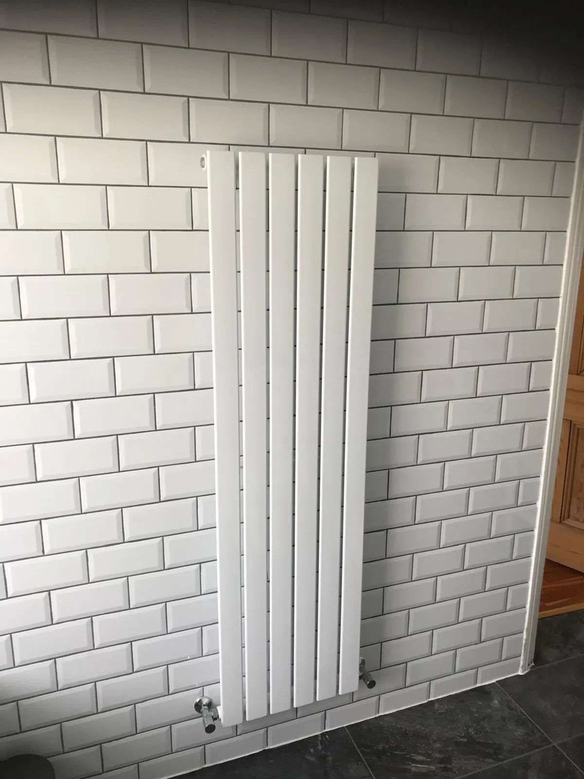 A white radiator next to a white brick wall.